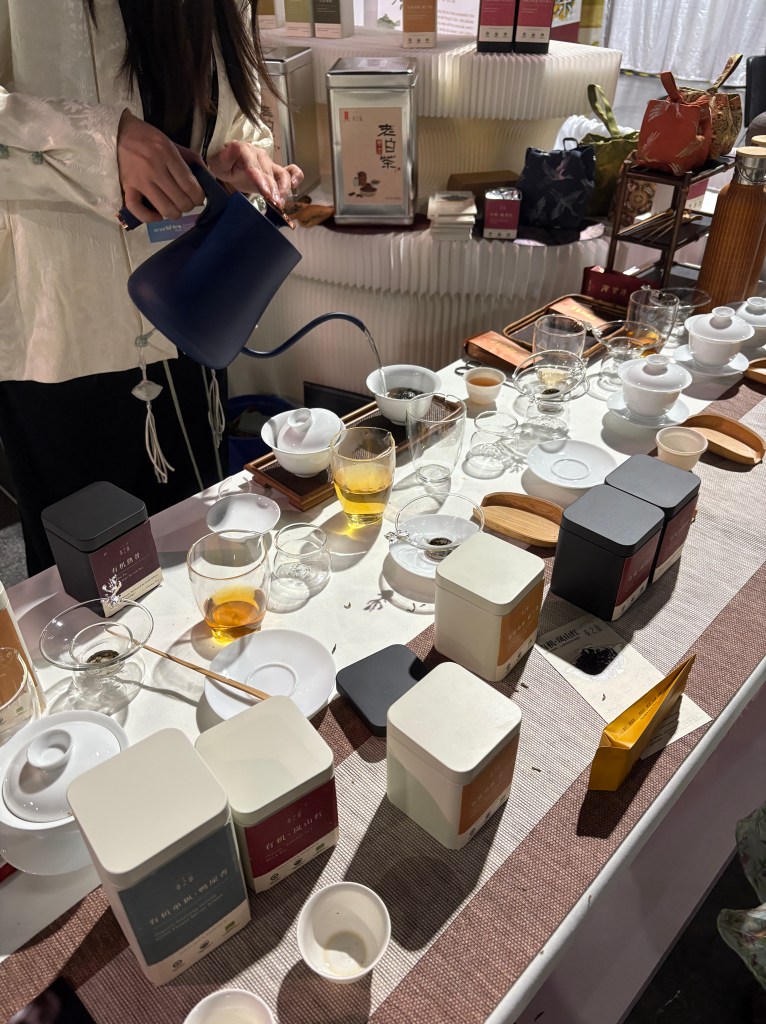 table filled with tea steeping gear and canisters of tea while a woman pours water and makes tea