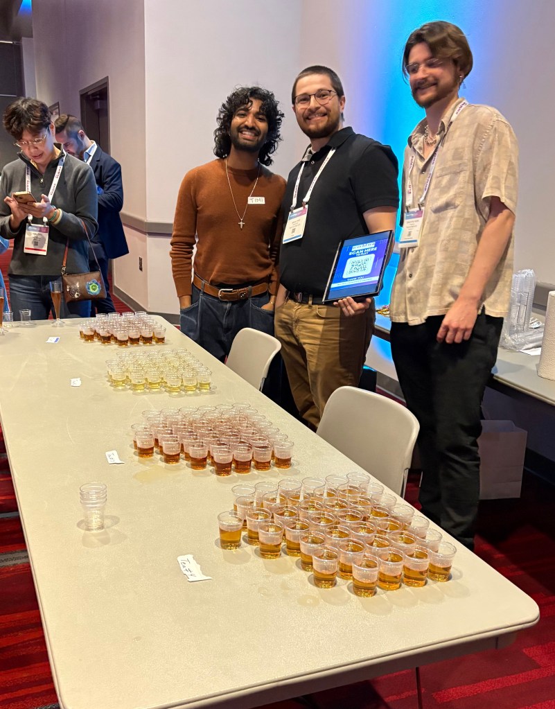 Three men standing in front of a table with tea tasting cups